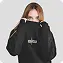 Woman with long light brown hair wearing a black oversized sweatshirt with the word euphoria printed in white gothic-style letters on the chest stands against a plain light gray background. She holds the collar of the sweatshirt with both hands, creating a relaxed and casual mood. The environment is minimalistic and modern with soft lighting and rounded corners. The text euphoria is clearly visible on the sweatshirt.
