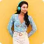 Woman with long dark wavy hair wearing turquoise headphones, a light blue patterned blouse, and high-waisted white pants with a brown belt stands against a bright yellow background with rounded corners. She has a relaxed posture, with one hand in her pocket, and a subtle, confident smile. The scene feels vibrant and modern, with a cheerful, energetic mood and no visible text in the image.