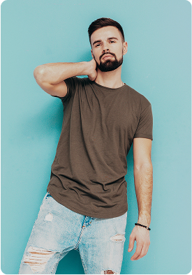 Man wearing a plain olive t-shirt and ripped light blue jeans stands in a relaxed pose against a solid light blue background with rounded corners. The setting feels modern and minimalistic, conveying a casual and confident mood. No visible text in the image.