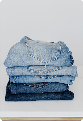 Stack of folded blue jeans in varying shades arranged neatly on a white surface with a light gray background and rounded corners. The setting feels clean and minimalistic, conveying a sense of order and simplicity. No visible text in the image.